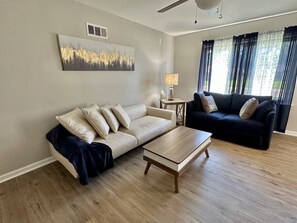 A living room with a beige sofa, a black sofa, a wooden coffee table, and a lamp on a side table. - Chic Central Retreat (Evansville)