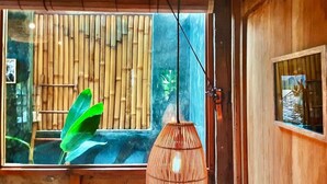 Een kamer met een groot raam, een bamboe wand en een hanglamp.