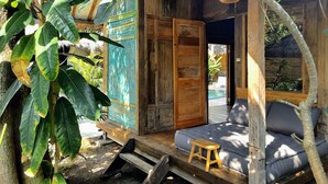 Een houten hut met een veranda, een klein houten krukje en een comfortabele zithoek.