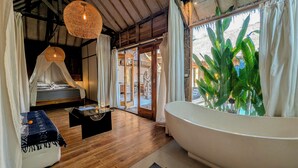Een kamer met een bed, een glazen bijzettafeltje, een groot bad en uitzicht op de omgeving.