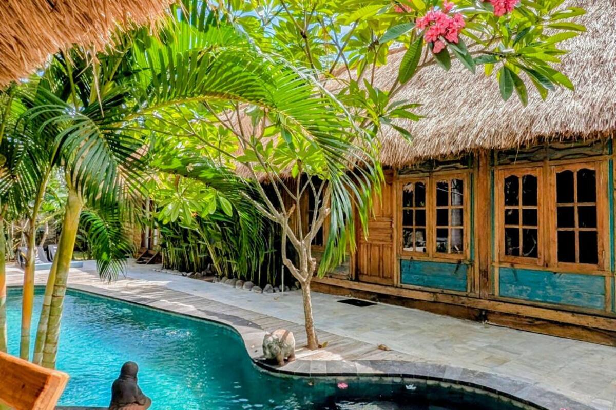 Un espace piscine agrémenté d’un abri au toit de chaume, entouré d’une végétation luxuriante et de palmiers.