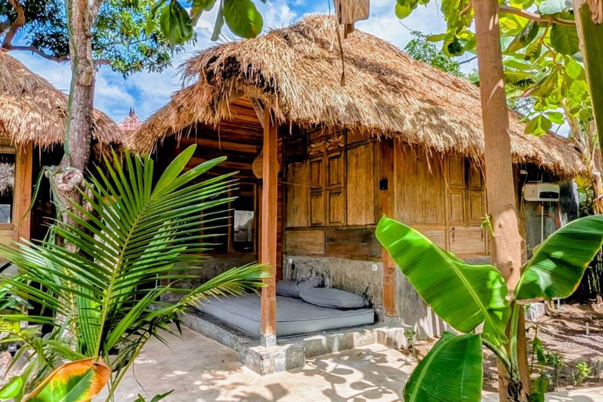 Une construction rustique en bois, dotée d’un toit de chaume, d’un petit porche et d’un espace de couchage avec un matelas.