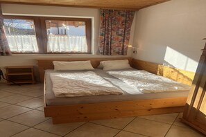 Un lit en bois avec une literie blanche, une fenêtre ornée de rideaux en dentelle et une table de chevet en bois.