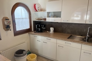 A kitchen with white cabinets, a wooden countertop, a coffee maker, a kettle, and a window with lace curtains.