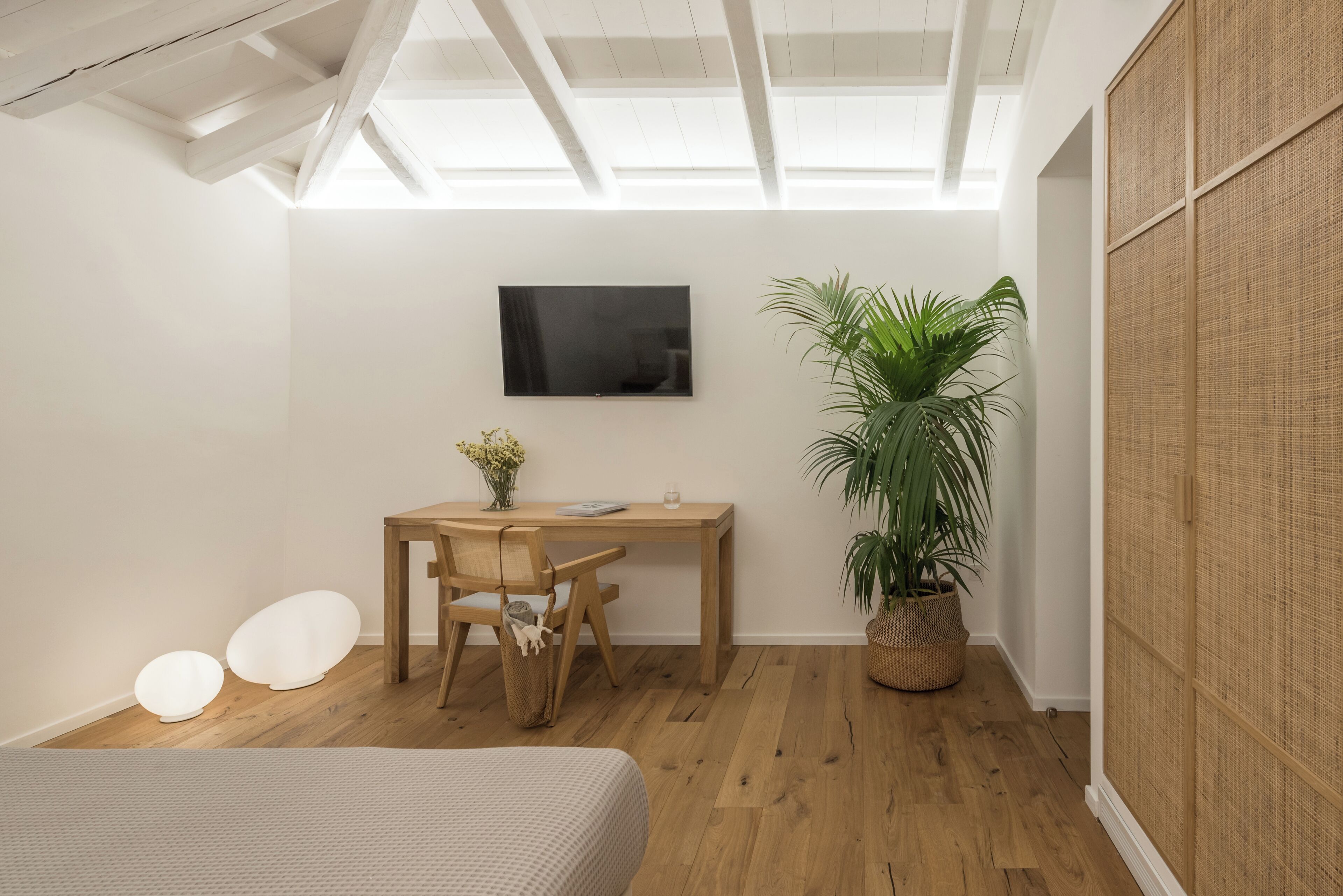 A modern bedroom with a skylight, a wooden desk, a chair, a bed, and a large potted plant.