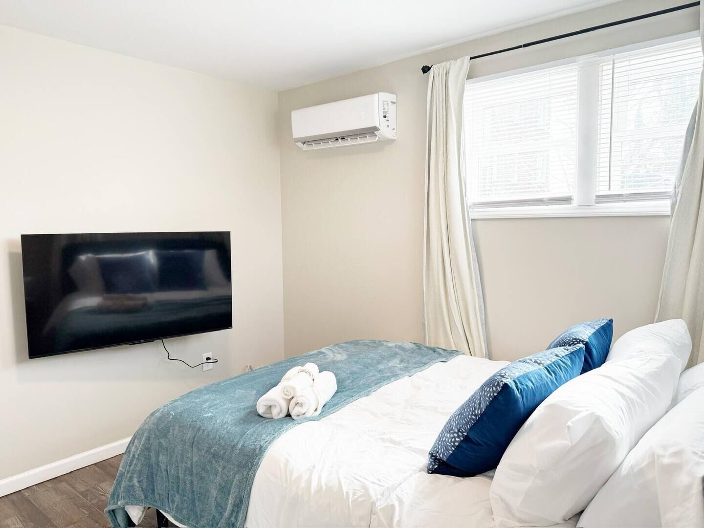 Una habitación de hotel con una cama, un televisor montado en la pared y un equipo de aire acondicionado.