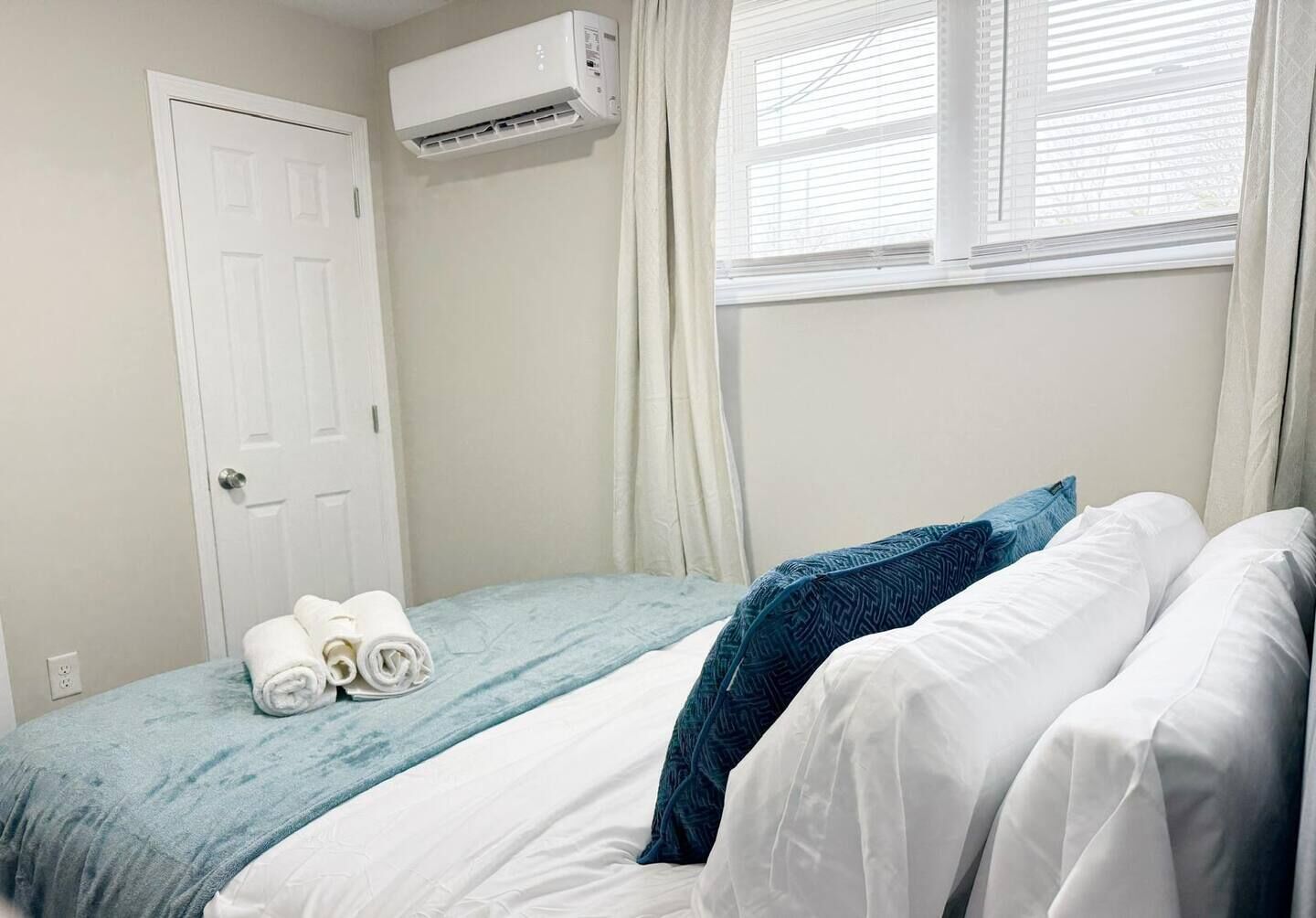 Un dormitorio con cama, ventana con persianas, unidad de aire acondicionado y puerta.