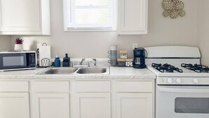 A kitchen with white cabinets, a microwave, a sink, a coffee maker, and a stove.