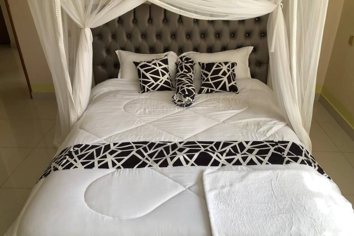 Una cama con cabecera capitonada, ropa de cama blanca y almohadas de estampado geométrico.