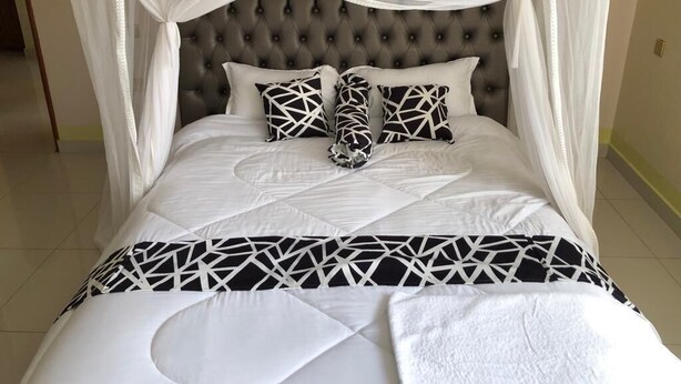 A bed with a tufted headboard, white bedding, and geometric-patterned pillows. - Villa Esperanza Kitui (Kitui)