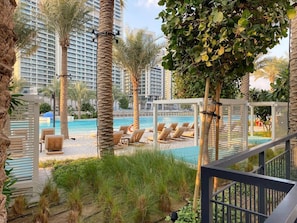 A poolside area with lounge chairs and palm trees. - FIRST CLASS | 1BR | Vida Creek Beach Bliss (Dubai Creek Harbour)