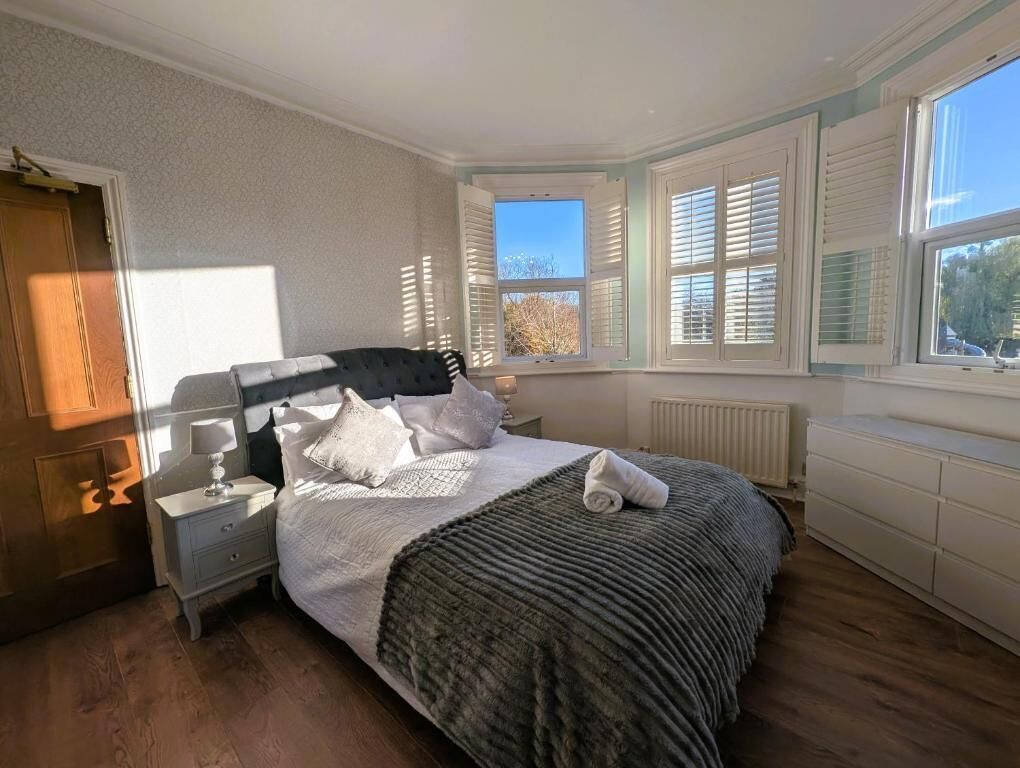 A bedroom with a bed, nightstands, a window with shutters, and a radiator.