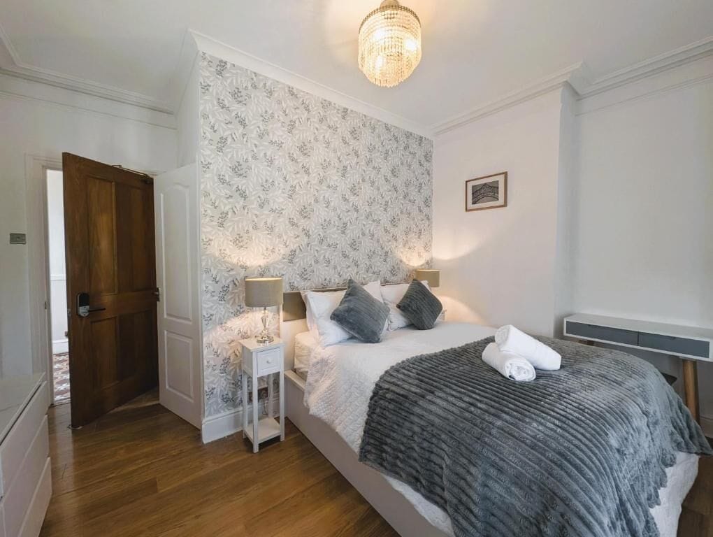 A bedroom with a bed, bedside lamps, a wooden door, and a patterned wallpaper.