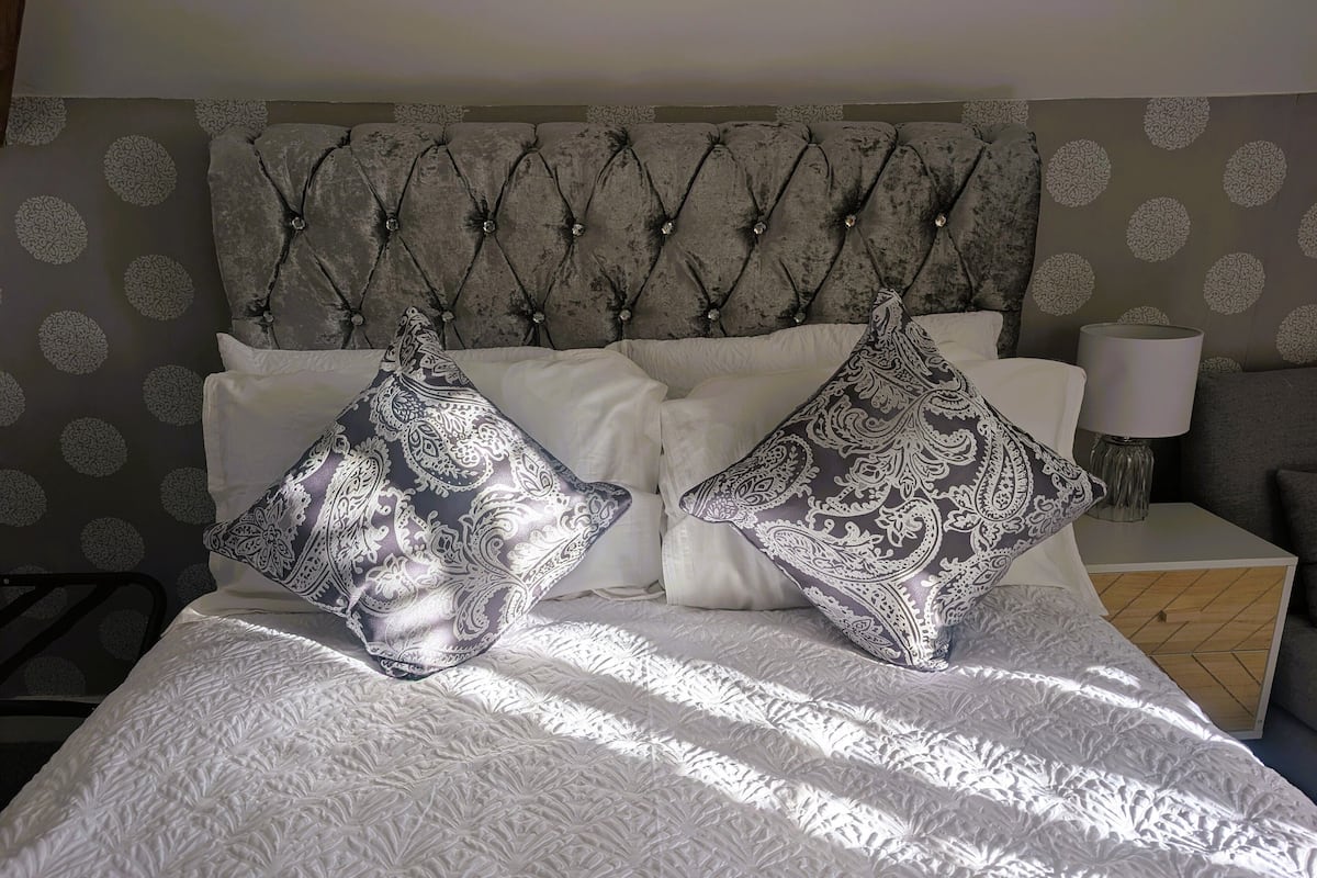 A bed with a tufted headboard, white bedding, and patterned pillows.