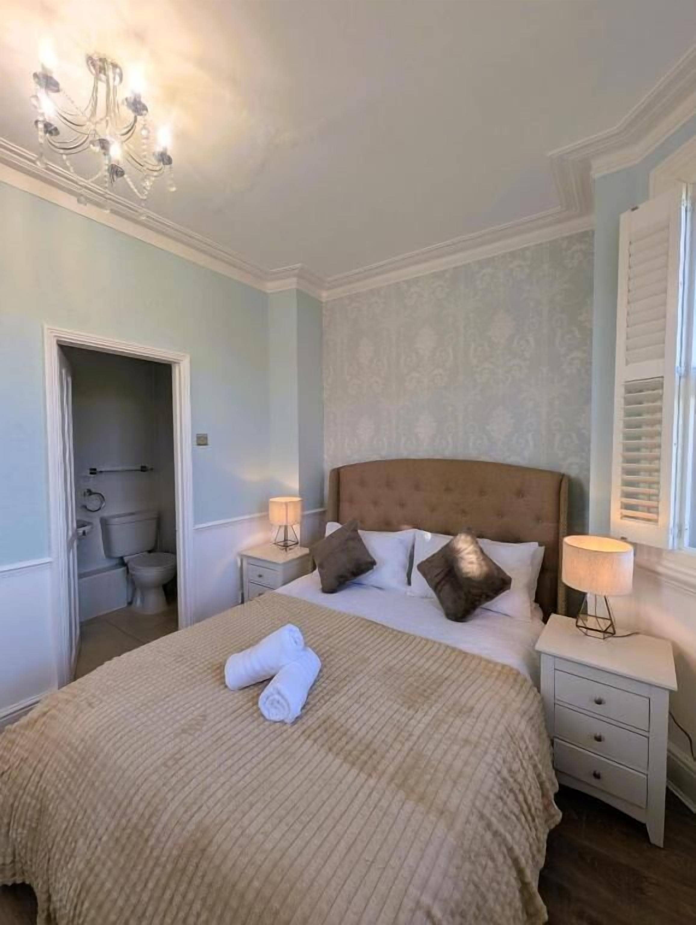 A neatly made bed with a brown headboard, two bedside tables with lamps, and a chandelier.