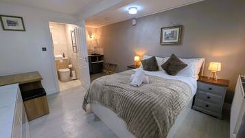A bedroom with a bed, bedside tables, a nightstand, a bathroom, and a small kitchenette.