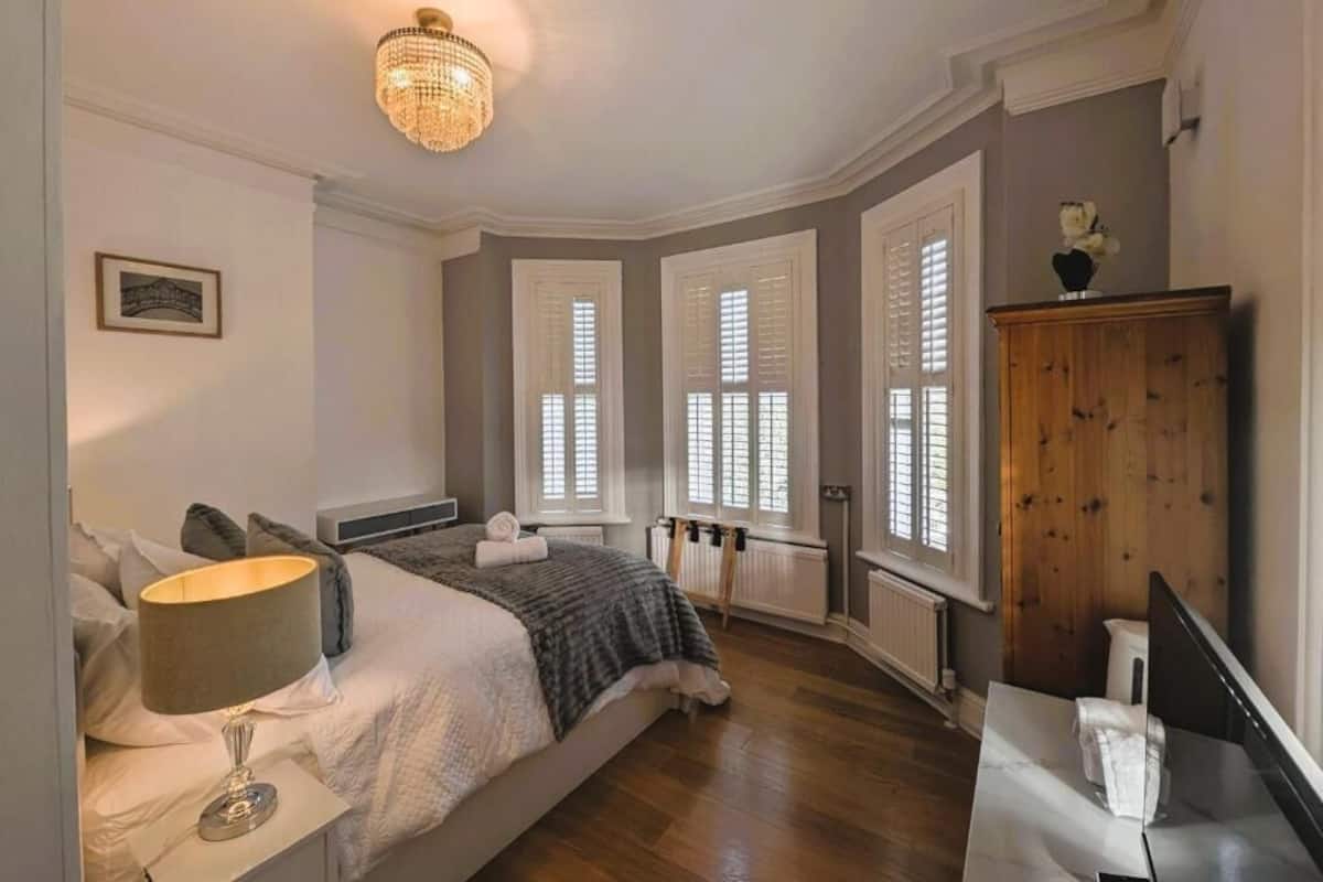 A bedroom with a bed, bedside table, lamp, dresser, and a chandelier.