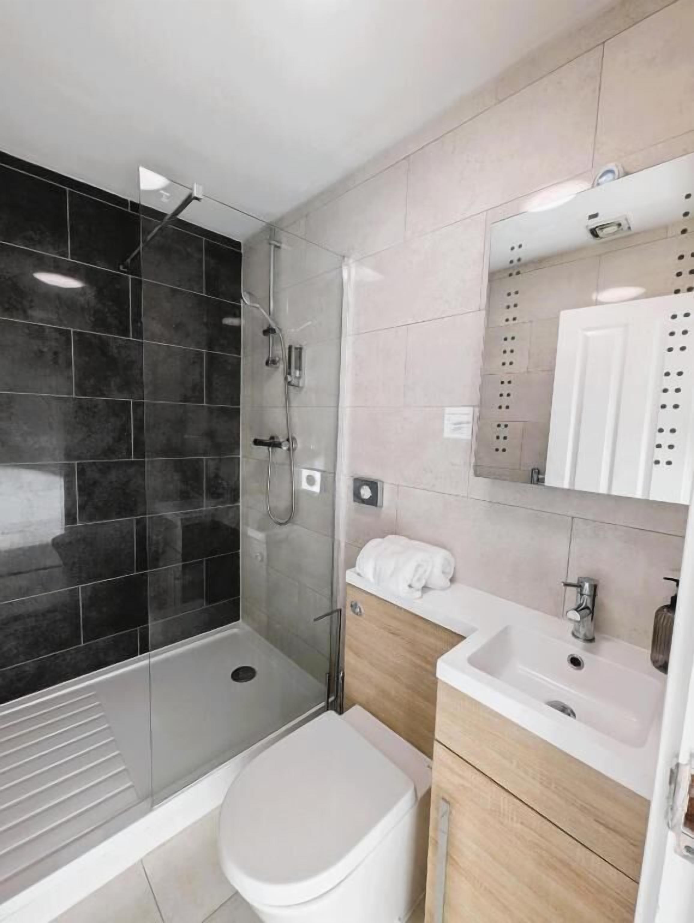 A modern bathroom with a glass-enclosed shower, a white toilet, a sink, and a vanity with a mirror.