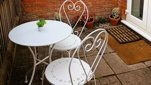 Un muro de ladrillo, una puerta blanca y un pequeño patio con una mesa y sillas.