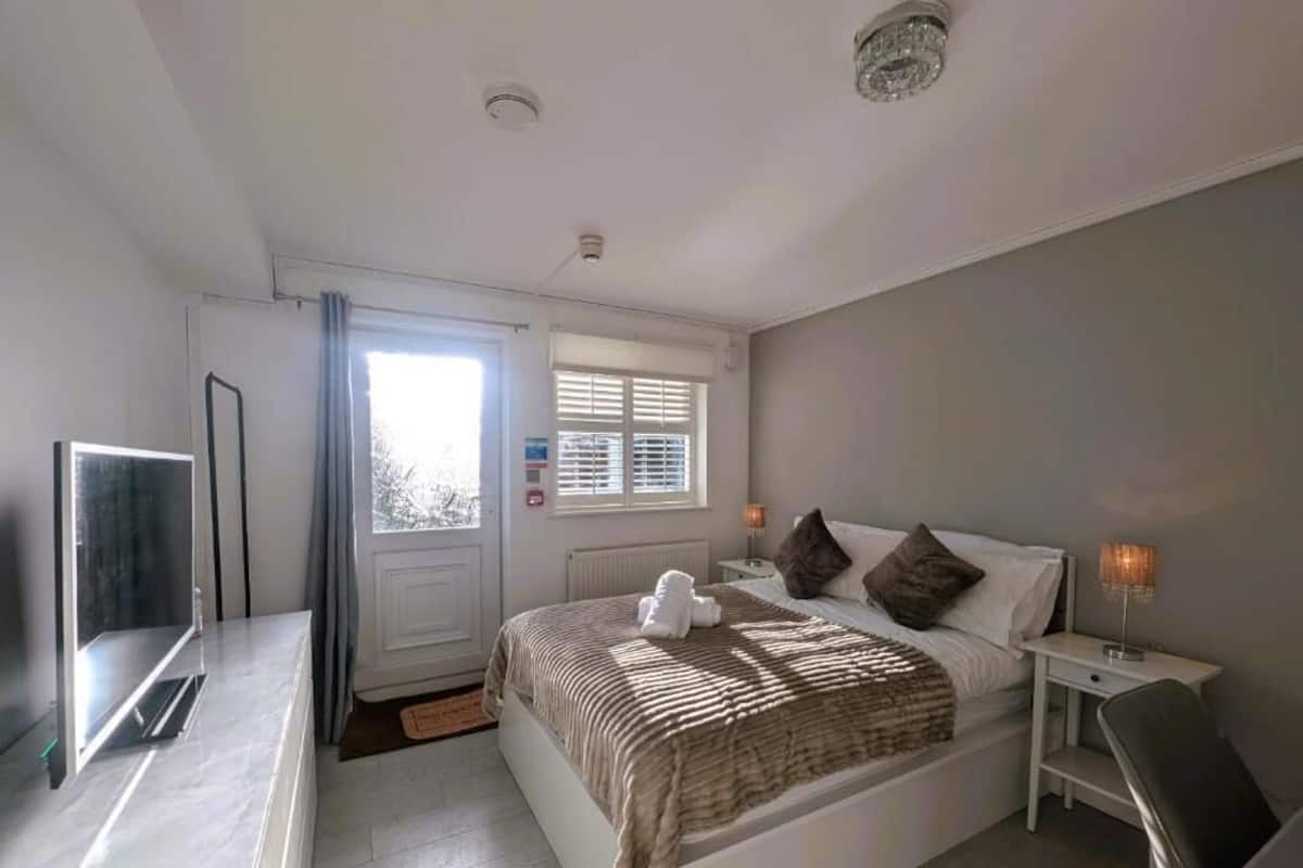 A bedroom with a bed, bedside tables, a TV, and a window with curtains.