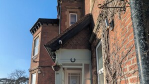 Un edificio de ladrillo de dos pisos con una puerta principal blanca, el número 118, y dos macetas con plantas en los escalones.