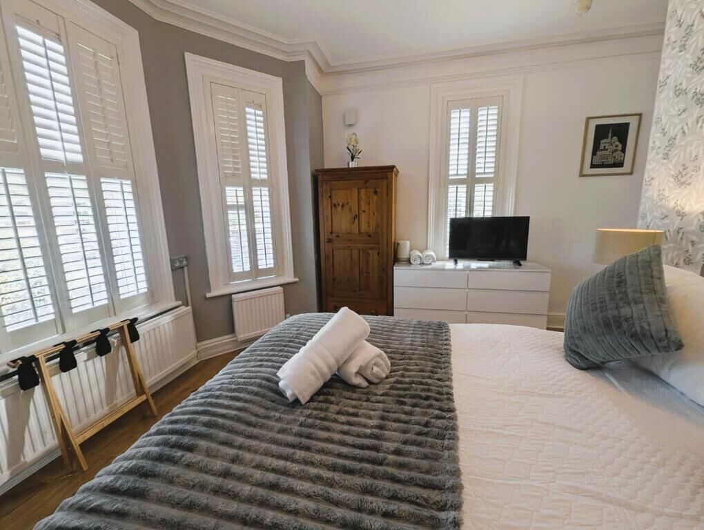 A bedroom with a large bed, a wooden wardrobe, a television, and a window with shutters.
