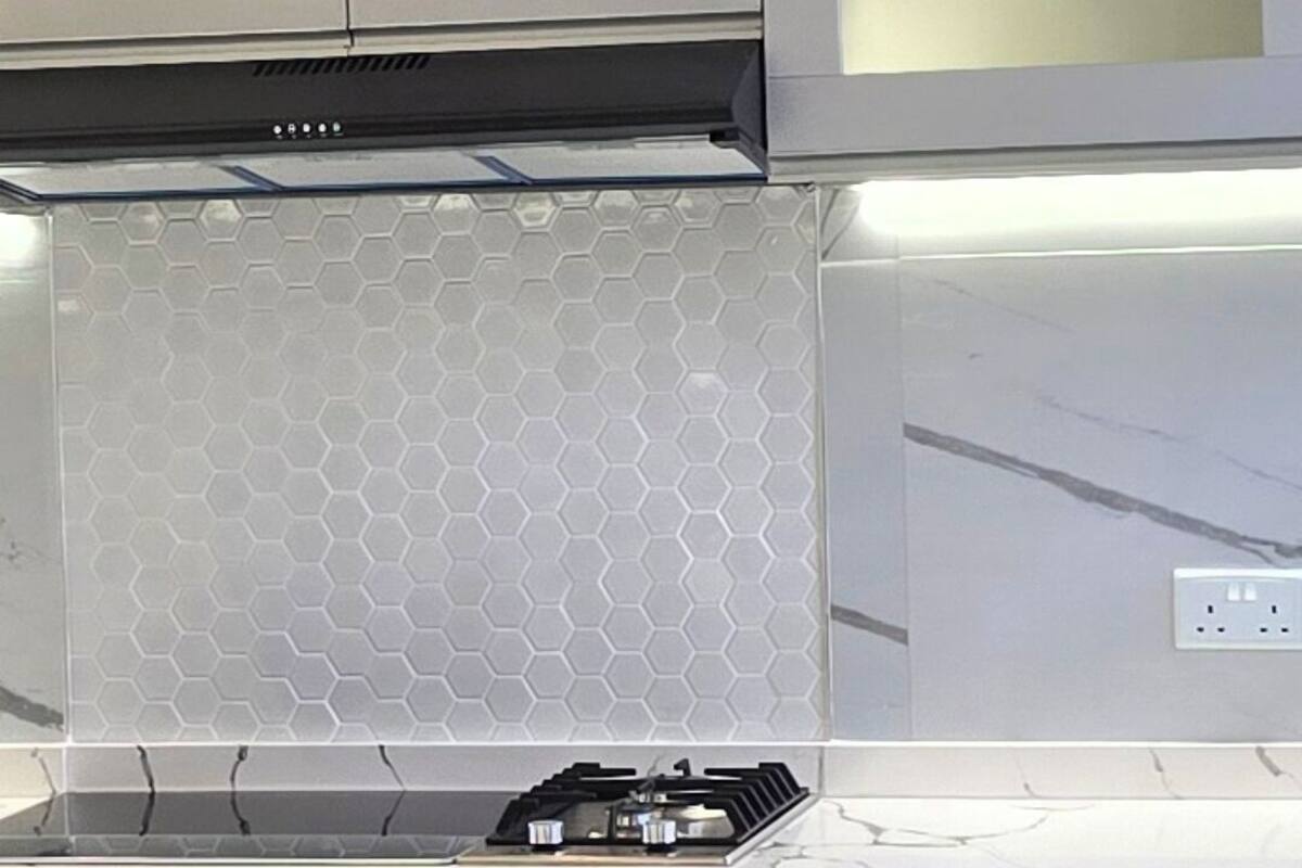 A modern kitchen with a hexagonal backsplash, a built-in stove, and upper cabinets with glass doors.