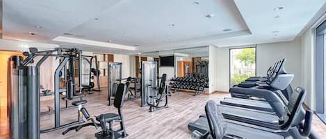 Une salle de sport équipée de divers appareils d’exercice, notamment des tapis de course et des appareils de musculation, ainsi qu’un grand miroir.
