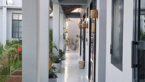 Un couloir aux murs blancs, doté d’un sol carrelé et agrémenté de plantes en pot.