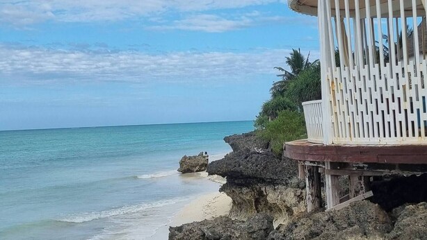 Une plage au terrain rocheux, avec une structure blanche dotée de lattes verticales.