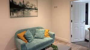Ein modernes Wohnzimmer mit einem petrolfarbenen Sofa, einem Couchtisch und einem Gemälde an der Wand.