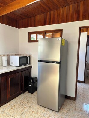 A kitchen with a stainless steel refrigerator, a microwave, and a trash bin. - Charming 3-Bedroom House Rental in Paquera, Costa Rica (Paquera)