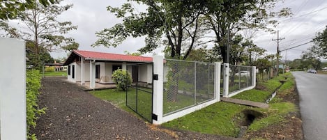 A fenced property with a small building, gravel driveway, and a road in the background.