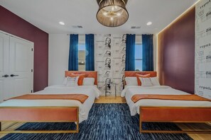 Een slaapkamer met twee bedden, een kroonluchter, een behang met patroon en een deur.