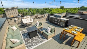 Une terrasse sur le toit aménagée avec un ensemble de canapés, une table à manger avec de l’assiette, un barbecue et un fauteuil suspendu.