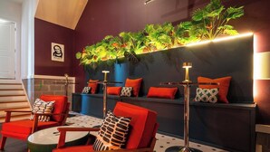 Un espace de détente moderne avec des fauteuils à revêtement rouge, une table ronde en verre et un présentoir à plantes fixé au mur.