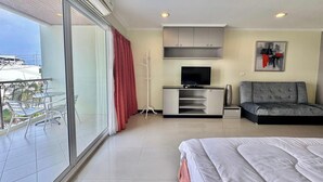 Ein modernes Hotelzimmer mit Balkon, einem Bett, einem grauen Sofa, einem Fernseher und einem Gemälde.
