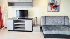 Ein modernes Wohnzimmer mit einem grauen Sofa, einem Flachbildfernseher auf einer weißen Unterhaltungsanlage und einem modernen abstrakten Gemälde an der Wand.