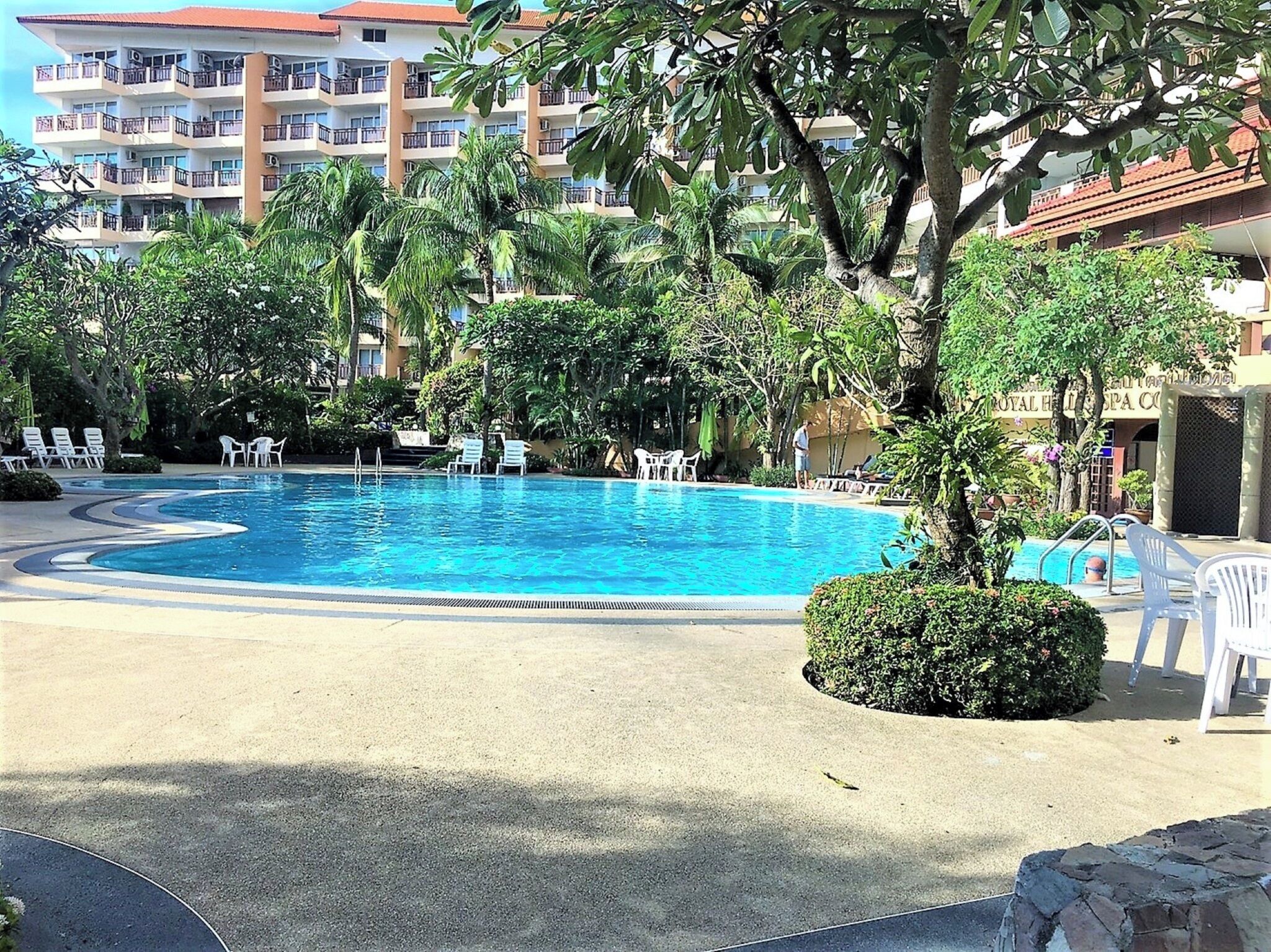 A swimming pool surrounded by lounge chairs and palm trees, with a hotel building in the background.