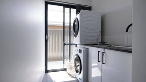 A compact laundry room with a front-loading washer and dryer, a small countertop, and a sliding glass door leading to an outdoor area.