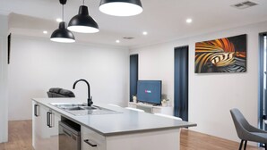 A modern kitchen with a central island, black pendant lights, and a flat-screen TV on a stand.