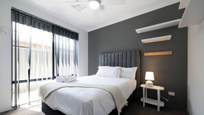 A modern hotel room with a large bed, a bedside table with a lamp, and a view of the outside through large windows.
