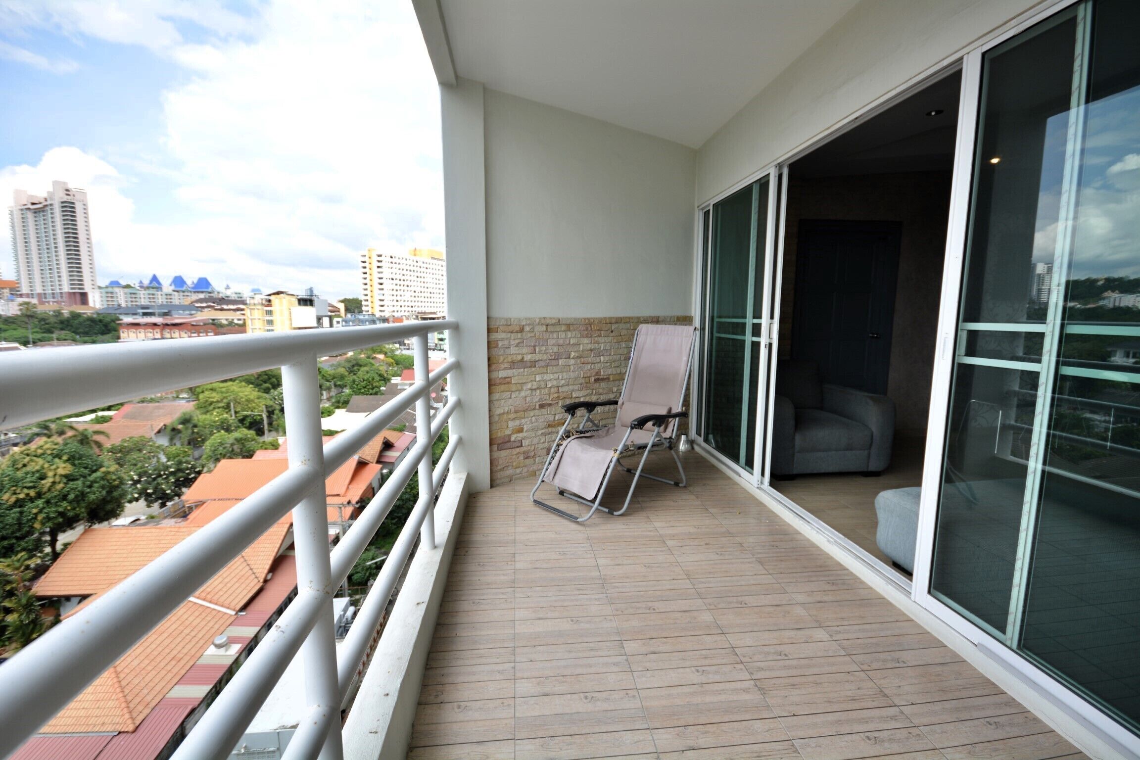 A balcony with a view of the city, a chair, and a glass door leading to an interior room.