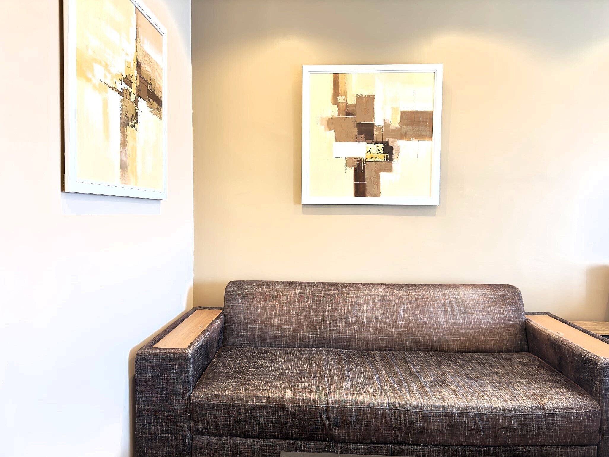 A modern living room with a dark brown sofa, a framed abstract painting, and a second painting on the wall.