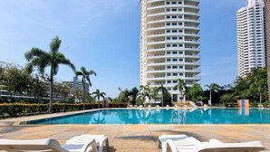 A swimming pool with lounge chairs, surrounded by palm trees and modern buildings. - Sea View Studio - Jomtien Beachfront - View Talay 8 (Muang Pattaya)