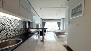 A modern hotel room with a kitchenette, a bed, a dining area, and a large window. - Sea View Studio - Jomtien Beachfront - View Talay 8 (Muang Pattaya)