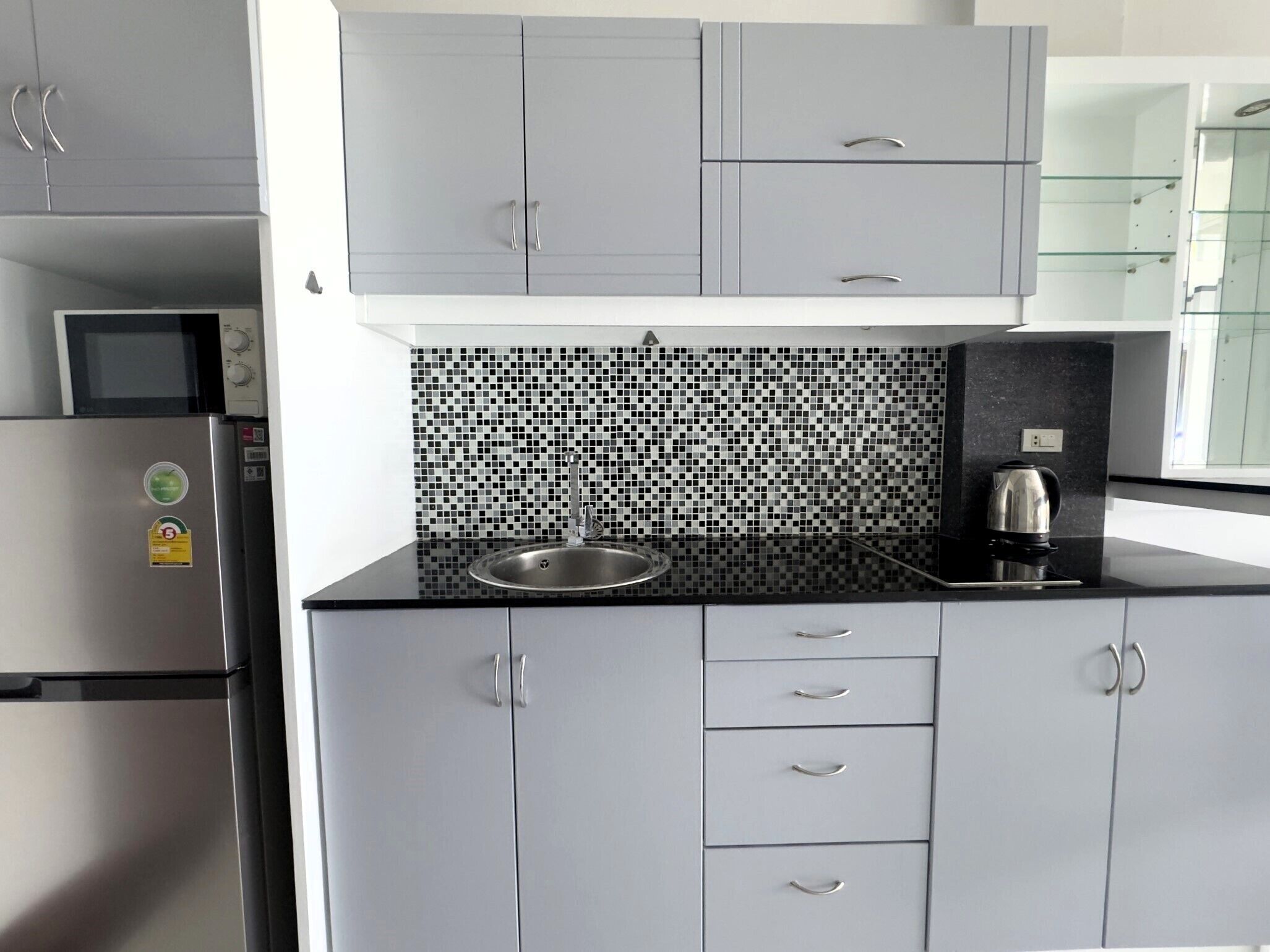 A modern kitchen with grey cabinets, a black and white tiled backsplash, and stainless steel appliances.