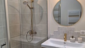 Une salle de bain moderne avec une douche à parois de verre, un miroir rond et un lavabo blanc avec un meuble en bois.