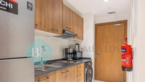 A modern kitchen with wooden cabinets, a stainless steel refrigerator, a coffee maker, and a washing machine. - Bloomfields Magnificent STU in Oasis (Abu Dhabi)