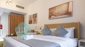 A hotel room with a large bed, a wooden wardrobe, a small table with a plant, and a painting on the wall. - Bloomfields Magnificent STU in Oasis (Abu Dhabi)